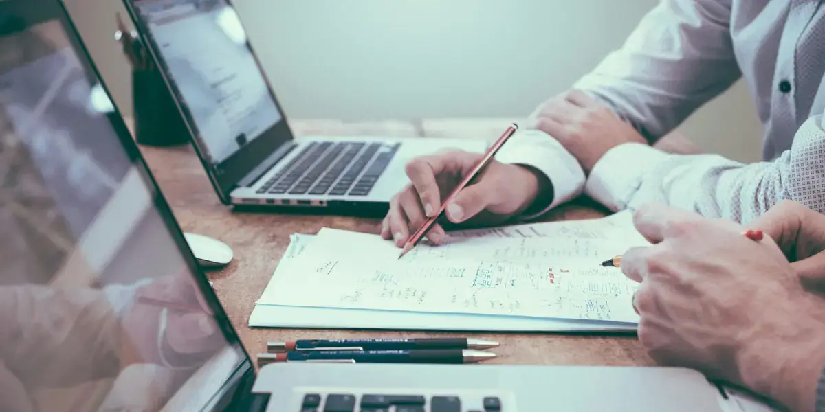 Dos personas dibujando la estructura de una web en un cuaderno junto a un portátil abierto